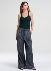 A woman modeling a dark green ribbed tank top and wide-leg pinstriped trousers in a studio setting with a light gray background.