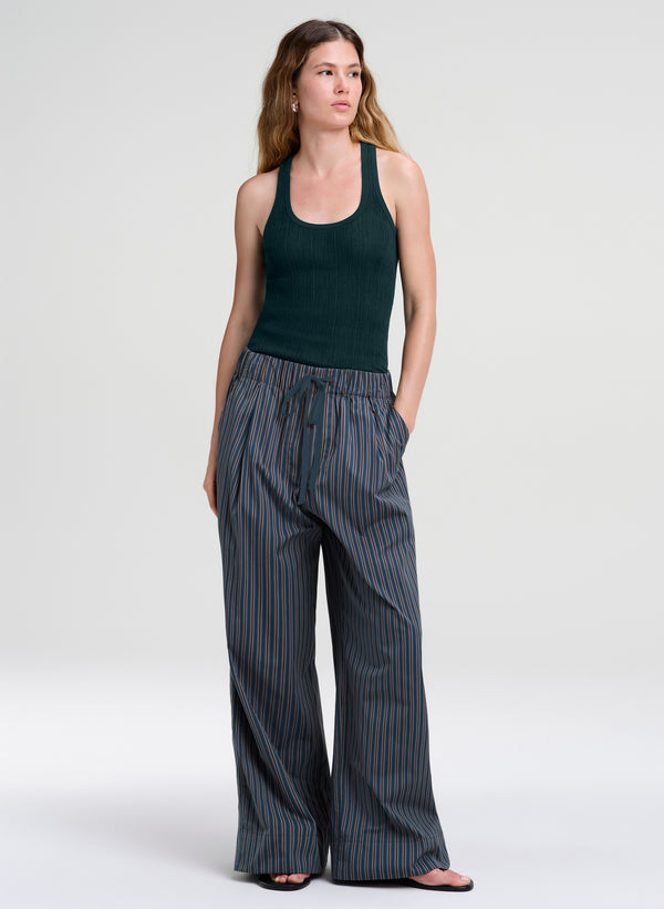 A woman modeling a dark green ribbed tank top and wide-leg pinstriped trousers in a studio setting with a light gray background.