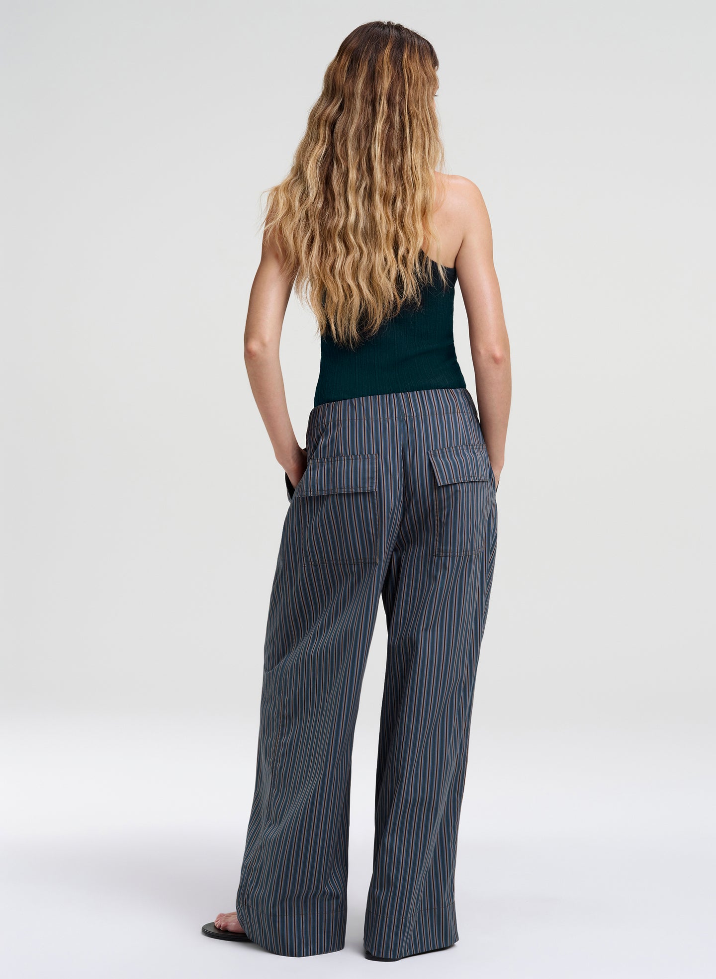 Woman wearing a green sleeveless top and pinstripe pants on a white background