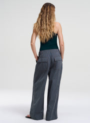 Woman wearing a green sleeveless top and pinstripe pants on a white background