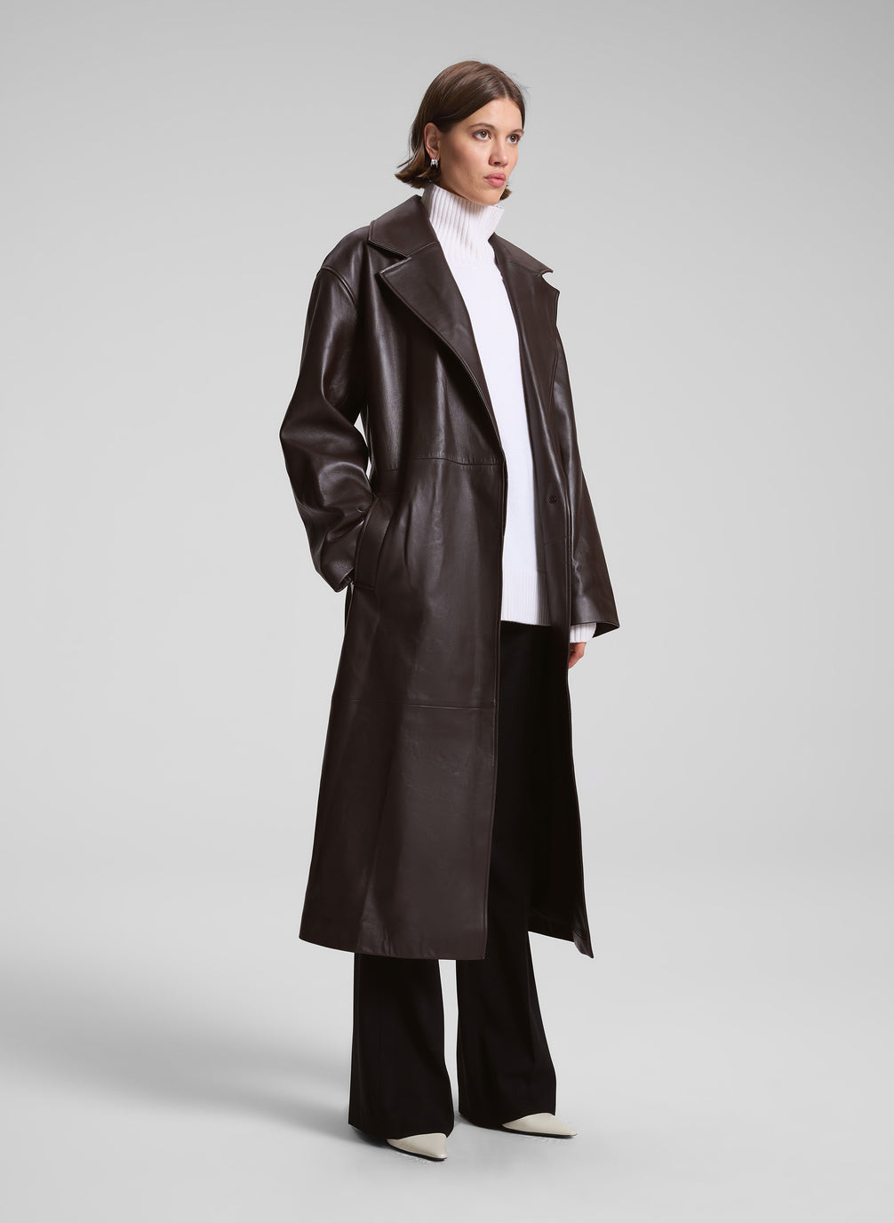 woman wearing brown leather coat, white sweater, and black pants