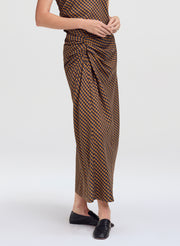 A model wearing a brown and black checkered wrap skirt with a gathered waist, paired with black flat shoes, against a light gray studio background.