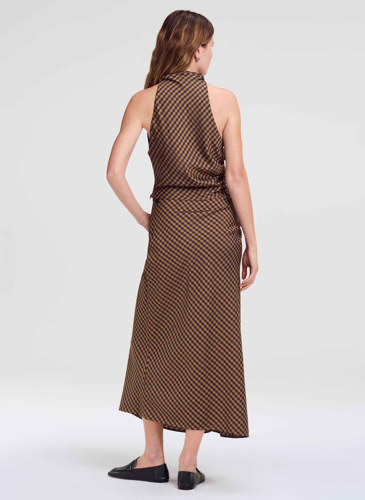 A woman shown from the back wearing a sleeveless top and matching skirt with a brown and beige geometric pattern, paired with black flats, against a light gray studio background.