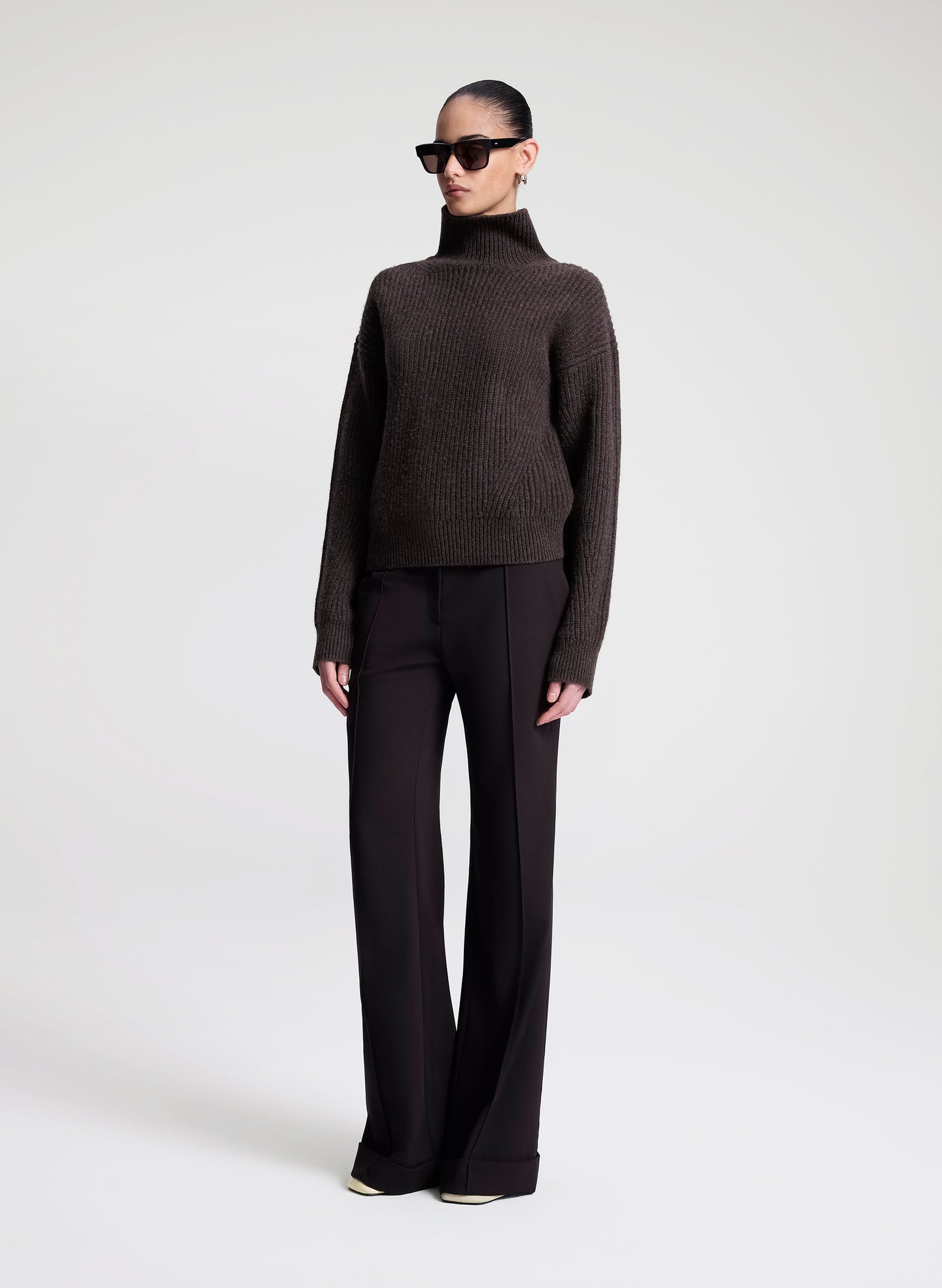 Person wearing a dark brown turtleneck sweater and black pants on a white background