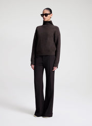 Person wearing a dark brown turtleneck sweater and black pants on a white background