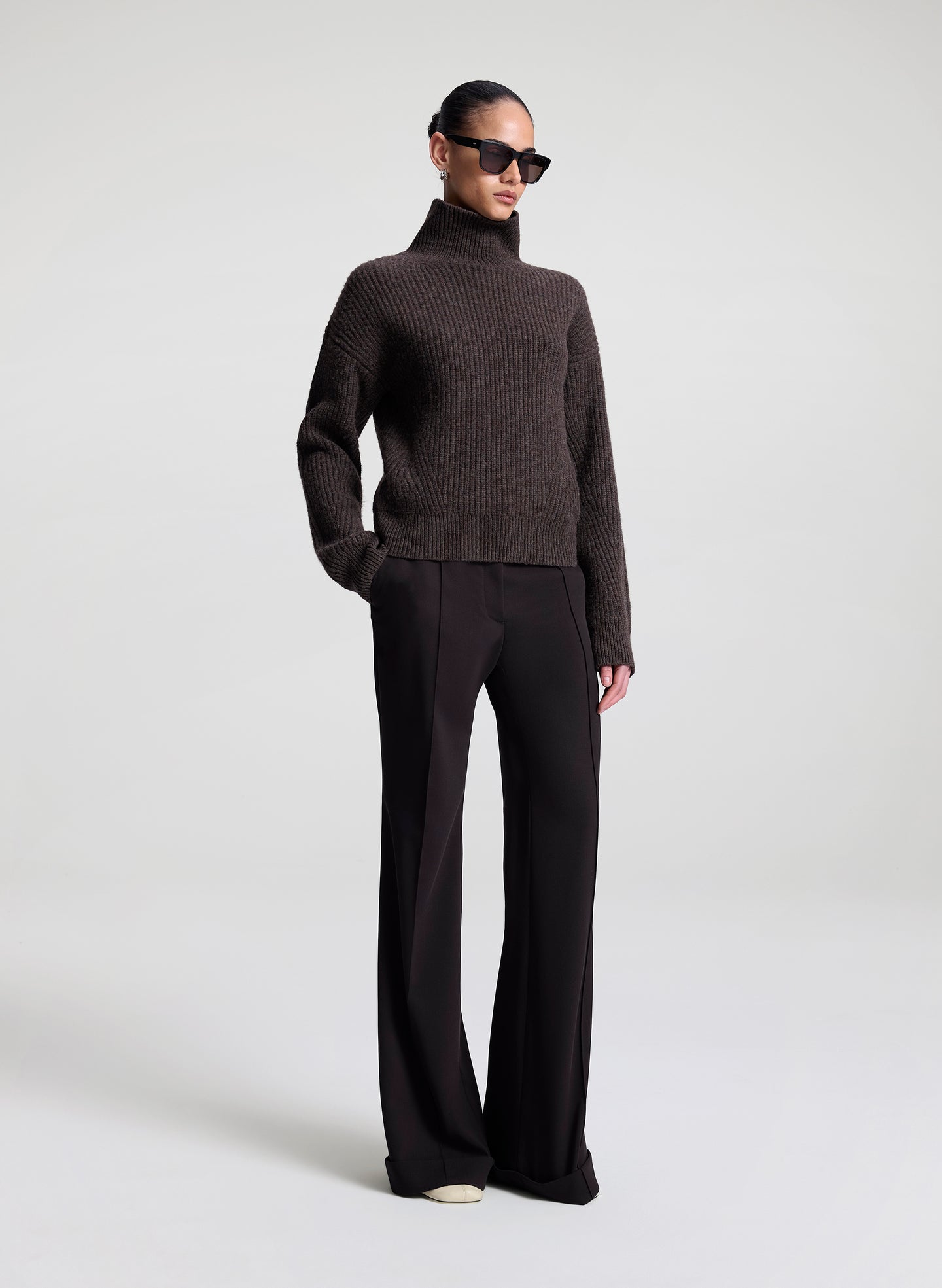 Person wearing a brown turtleneck sweater and black pants on a white background