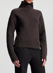 Brown ribbed turtleneck sweater worn by a person on a light gray background