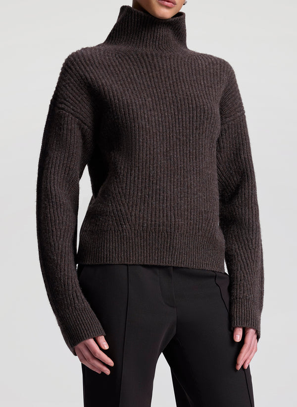 Brown ribbed turtleneck sweater worn by a person on a light gray background