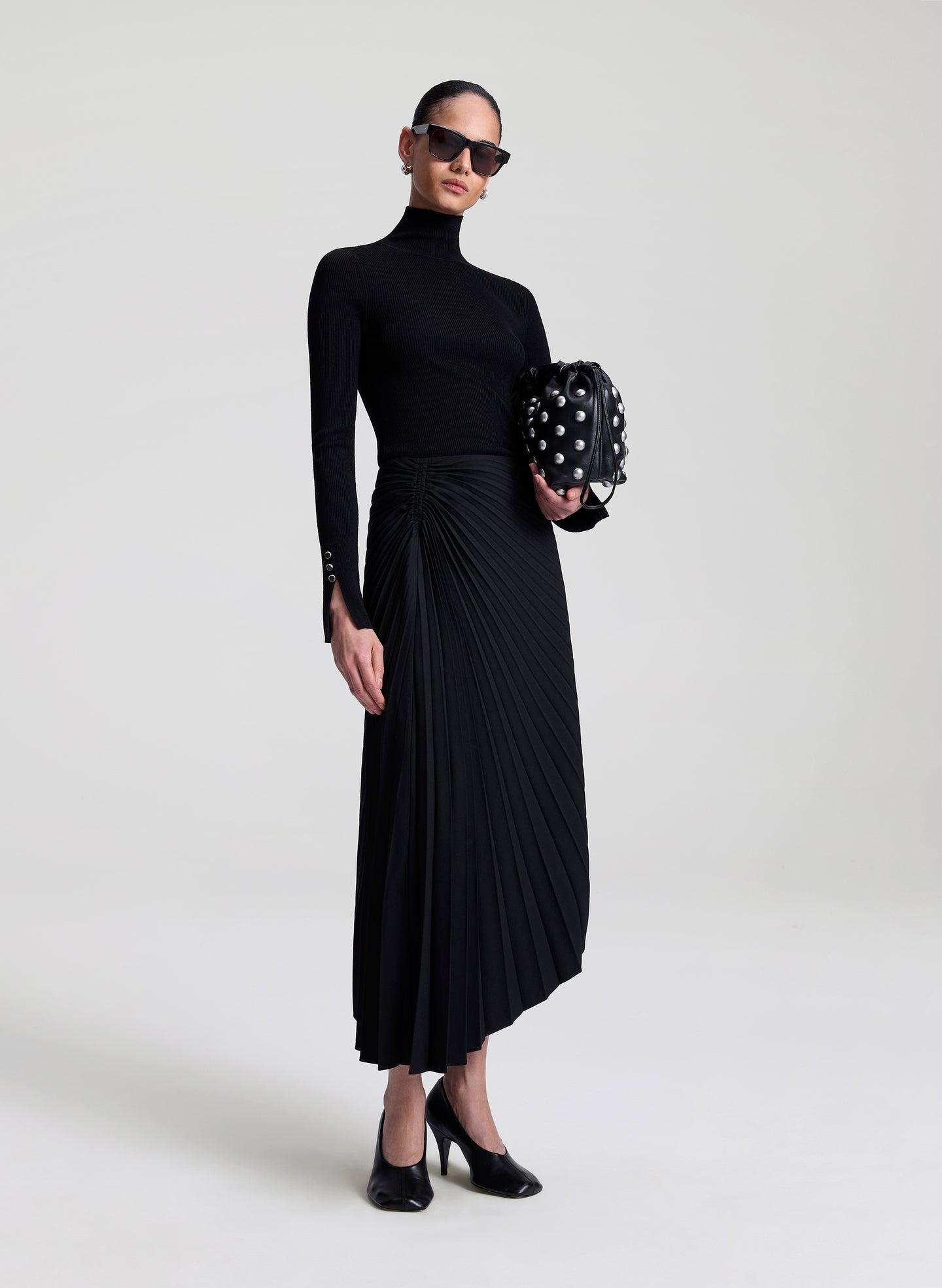 woman wearing black turtleneck and black pleated skirt