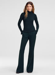 A woman modeling a dark green long-sleeve mock neck top and matching wide-leg trousers against a light gray studio background.