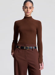 Person wearing a brown ribbed turtleneck and pants with a belt on a light gray background