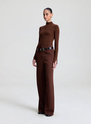 Person wearing a brown turtleneck and wide-leg pants on a white background