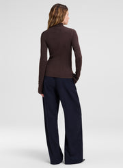 A woman shown from the back wearing a fitted dark brown mock-neck knit top and dark navy wide-leg trousers, photographed against a light gray studio background.