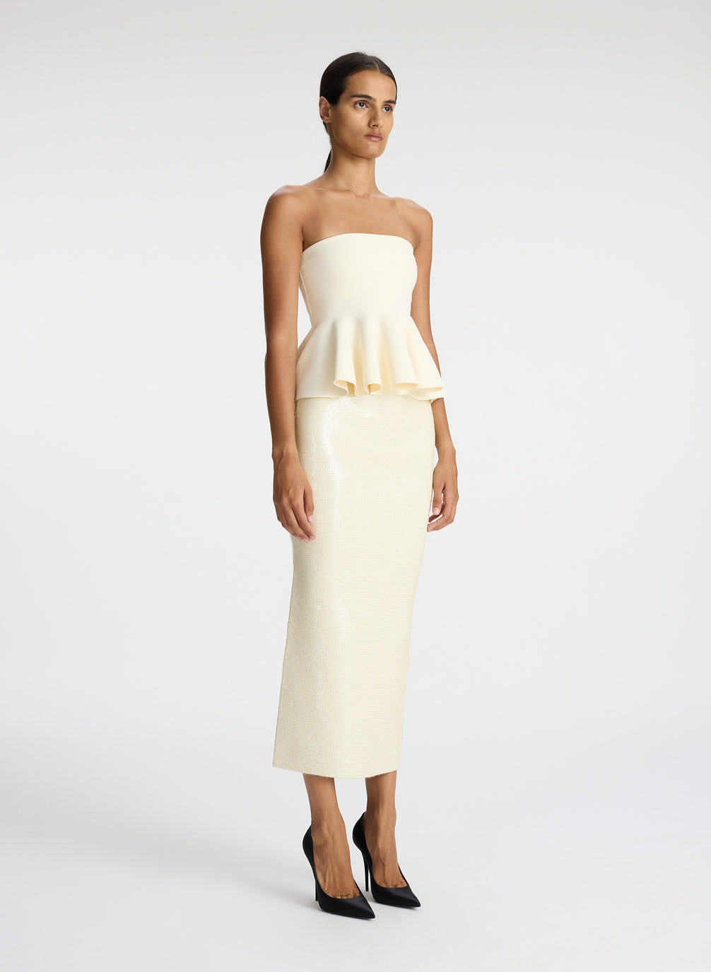 side view of woman wearing cream strapless peplum top and cream sequined midi skirt