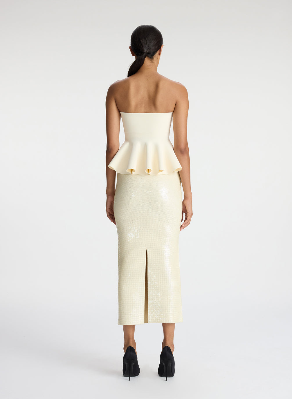 back view of woman wearing cream strapless peplum top and cream sequined midi skirt