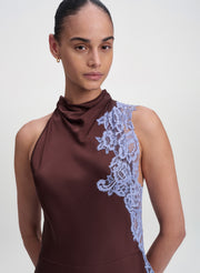 A model wearing a sleeveless high-neck dress in dark brown with a light blue lace panel on the side, shot against a plain light gray background.