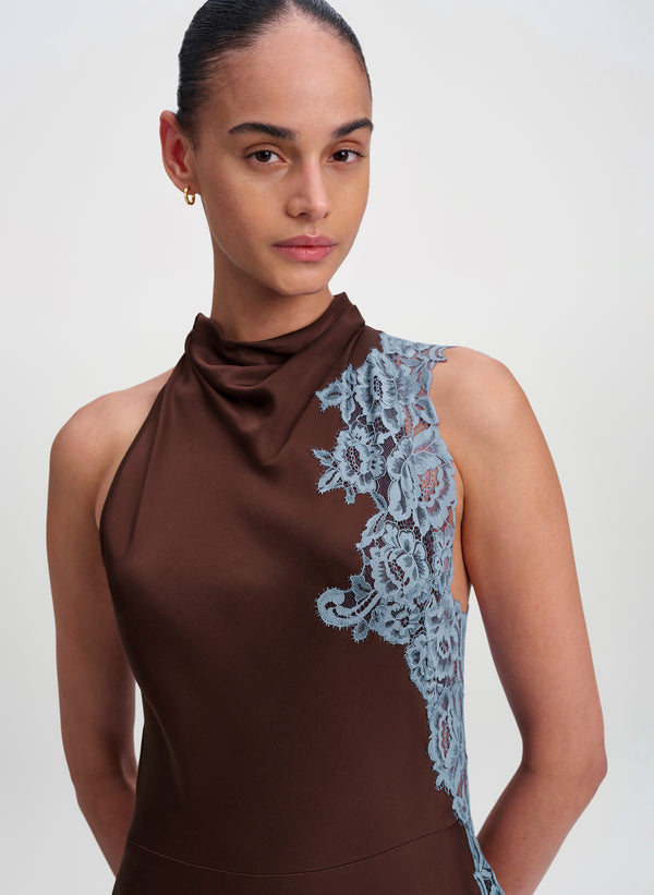 A model wearing a brown halter-neck dress with a light blue floral lace panel on the side, photographed against a plain light gray studio background.