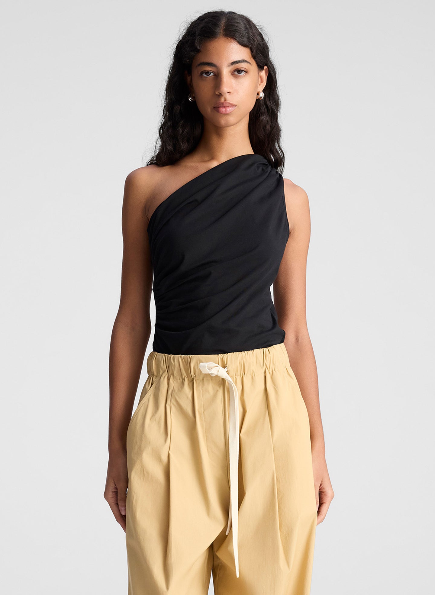 woman wearing one shoulder black tank and  tan wide leg pants