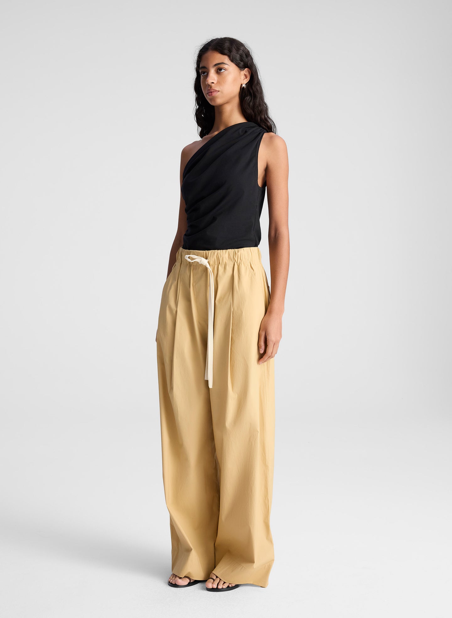 woman wearing one shoulder black tank and  tan wide leg pants