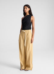 woman wearing one shoulder black tank and  tan wide leg pants