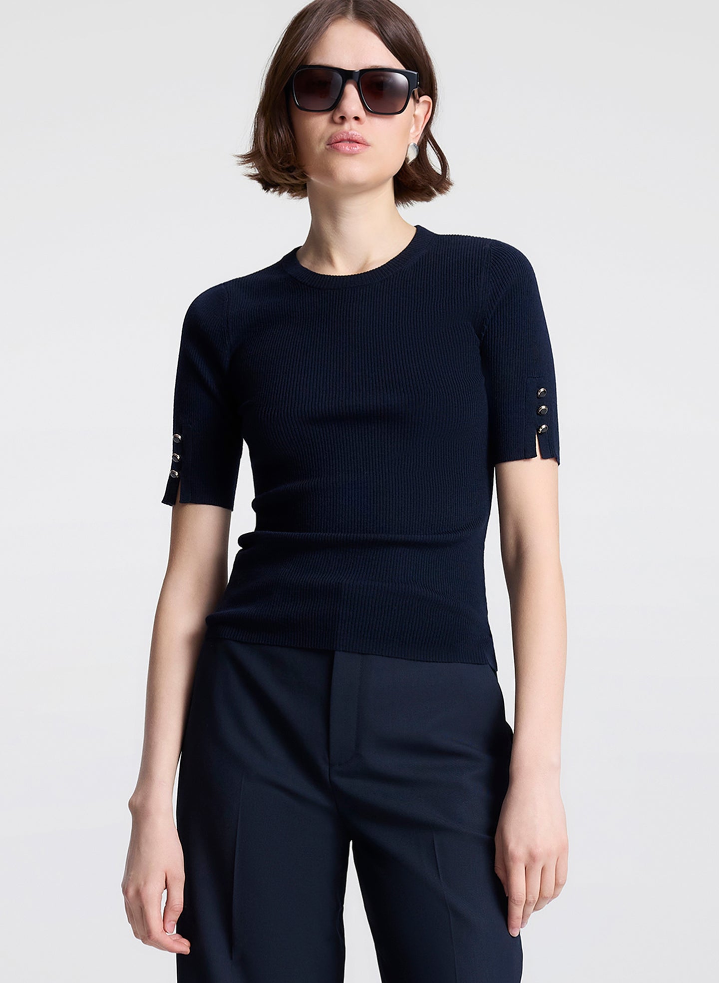 Person wearing a navy blue outfit with decorative sleeves on a light gray background