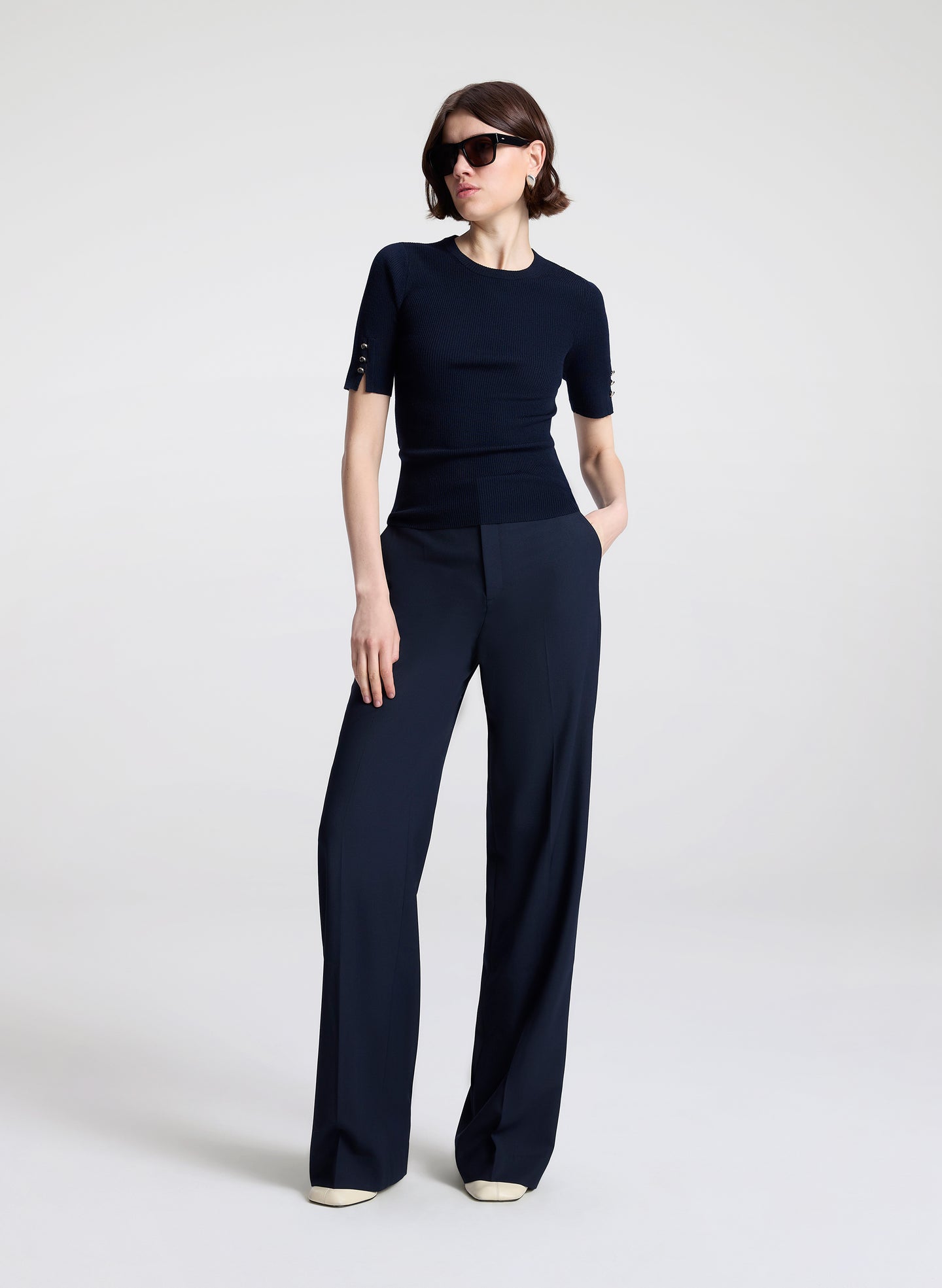 Woman wearing a navy outfit with sunglasses on a white background