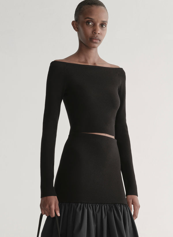 Woman wearing a black long-sleeve top and skirt set against a plain background