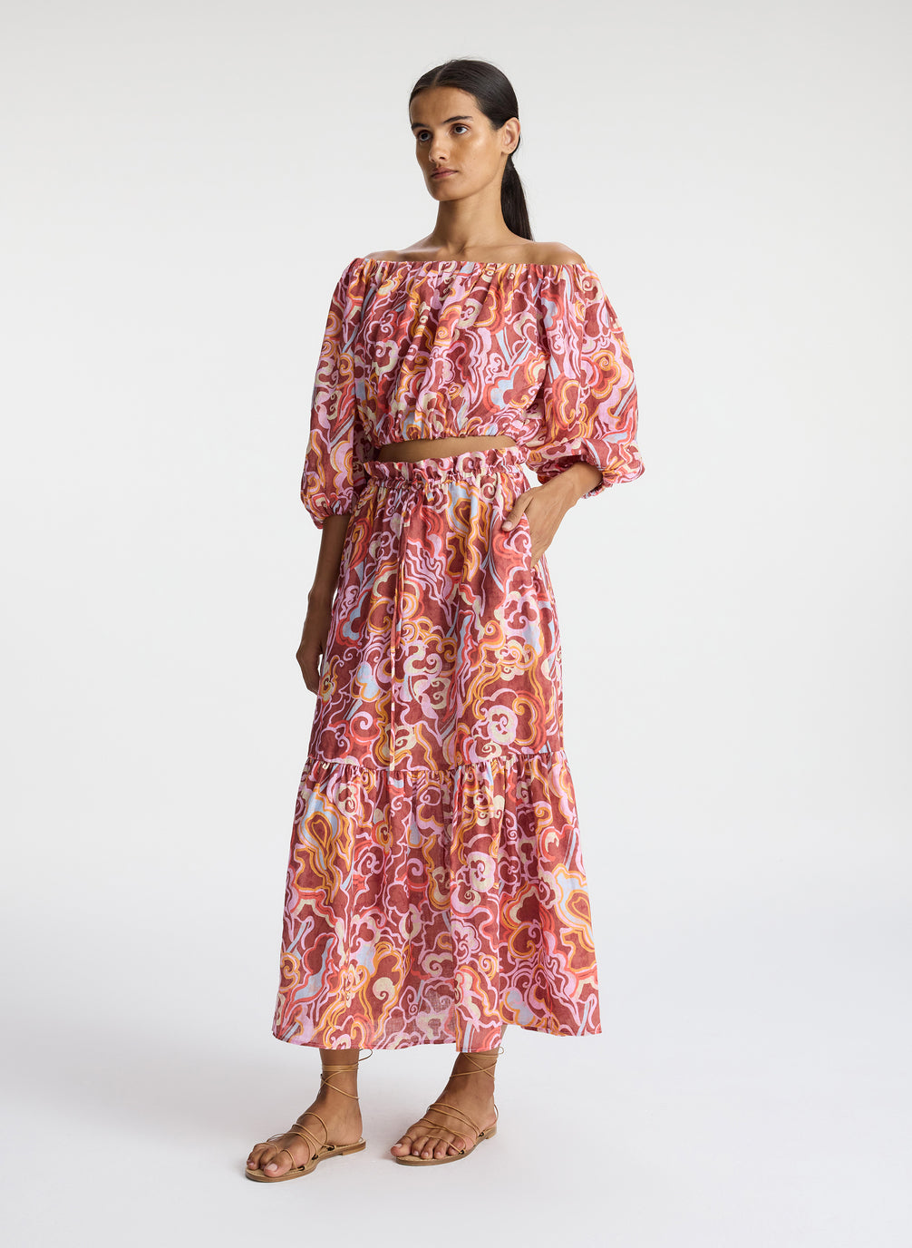 side view of woman wearing magenta and orange abstract print off shoulder top and matching midi skirt