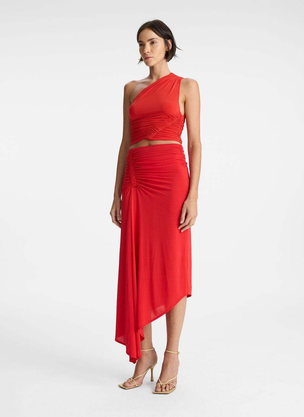 side view of woman wearing red one shoulder tank top and red ruched midi skirt