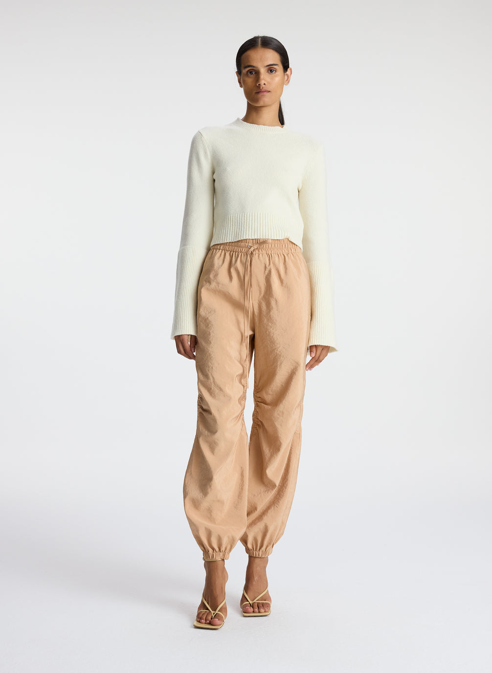 front view of woman wearing white sweater and beige nylon drawstring pants