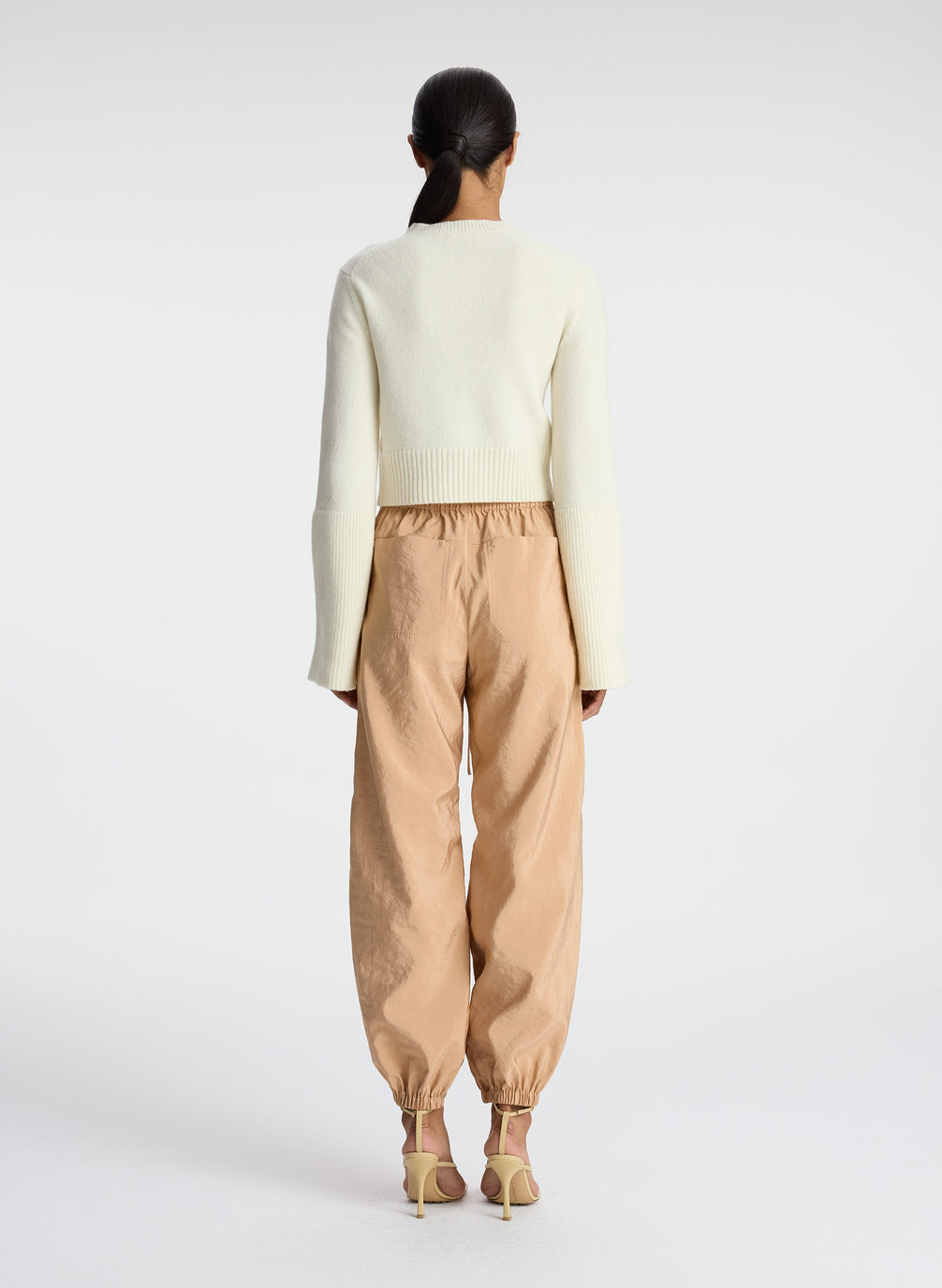 back view of woman wearing white sweater and beige nylon drawstring pants