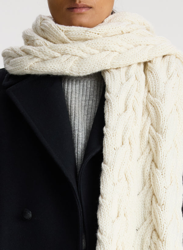 detail view of woman wearing cream cable knit scarf with fringe