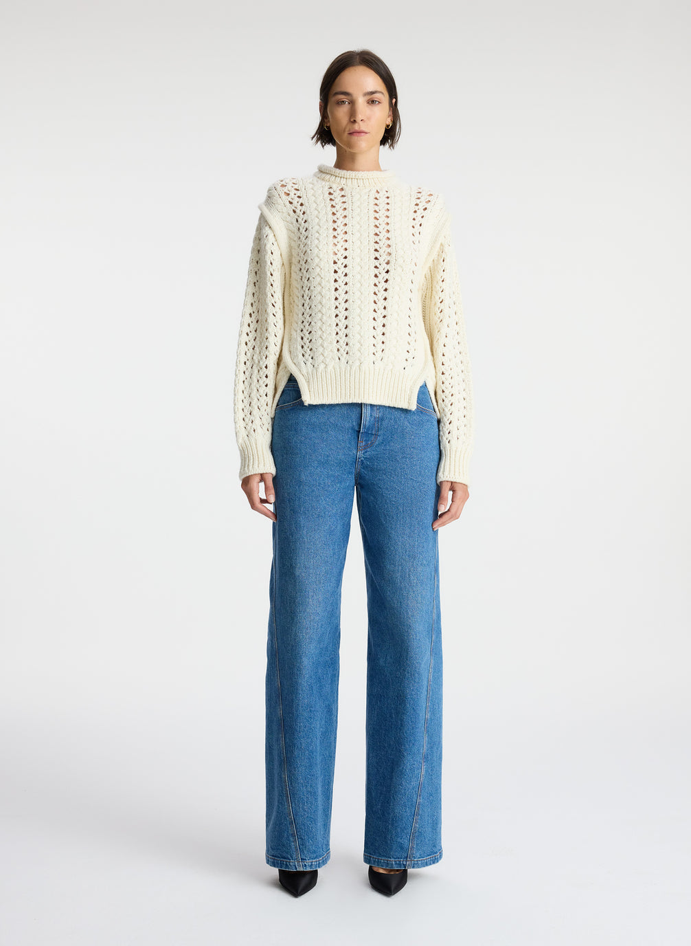 front view of woman wearing cream open knit sweater and medium wash denim jeans