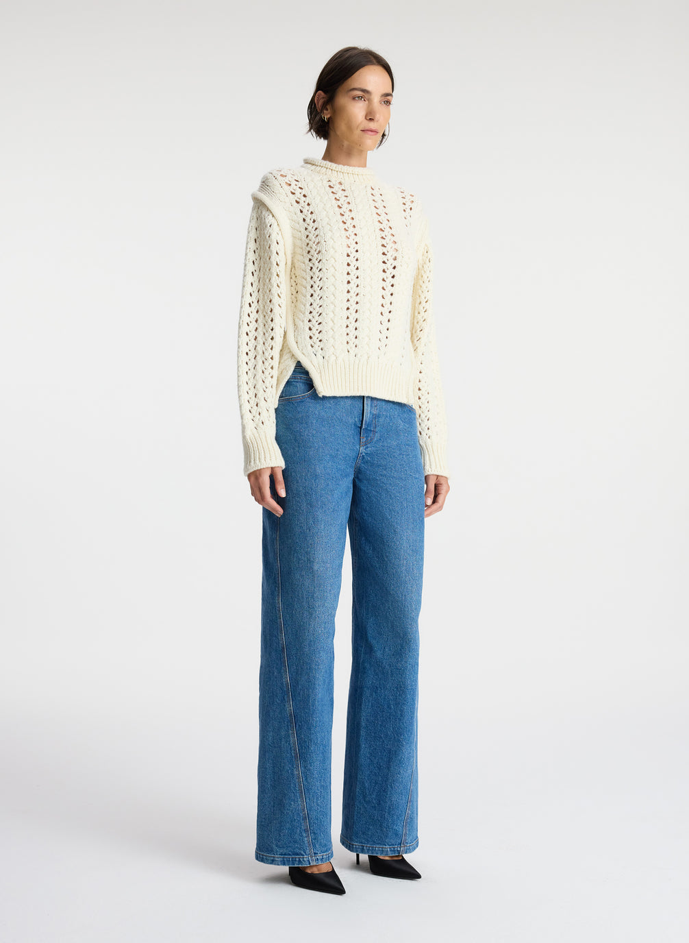 side view of woman wearing cream open knit sweater and medium wash denim jeans