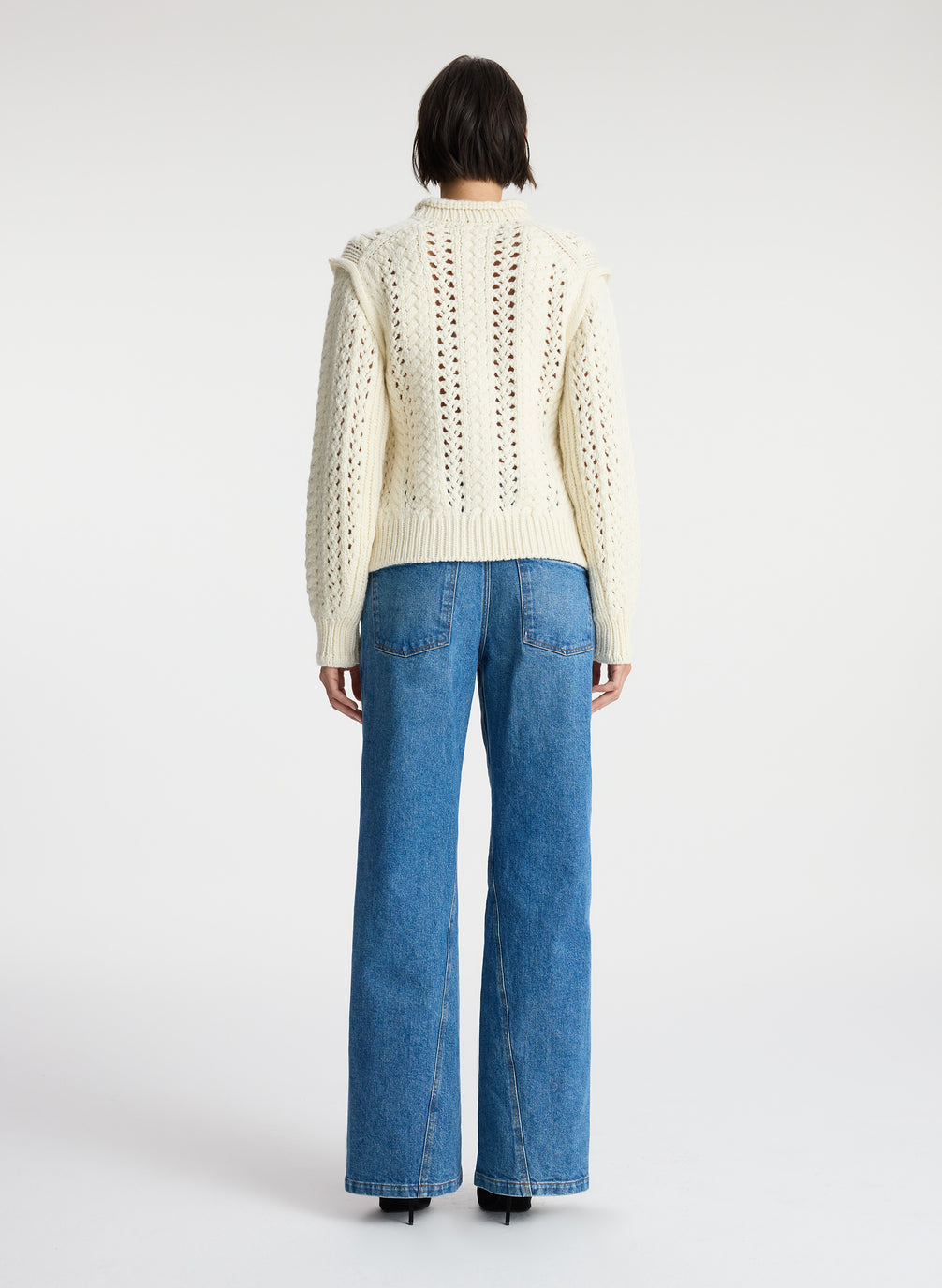 back view of woman wearing cream open knit sweater and medium wash denim jeans