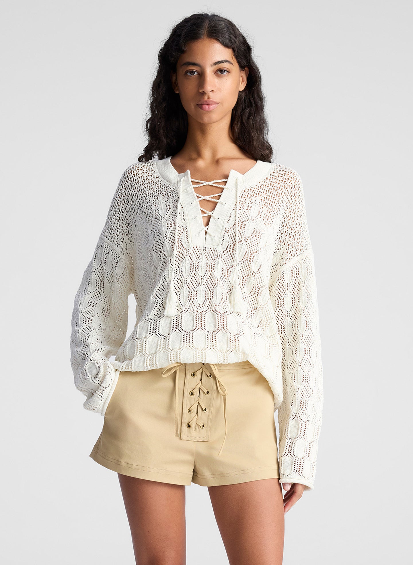 woman wearing white open knit pullover sweater and lace up detail beige shorts