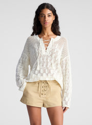 woman wearing white open knit pullover sweater and lace up detail beige shorts