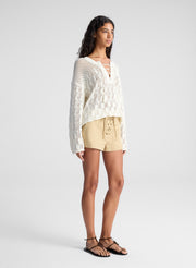 woman wearing white open knit pullover sweater and lace up detail beige shorts