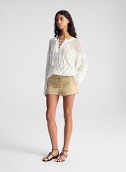 woman wearing white open knit pullover sweater and lace up detail beige shorts