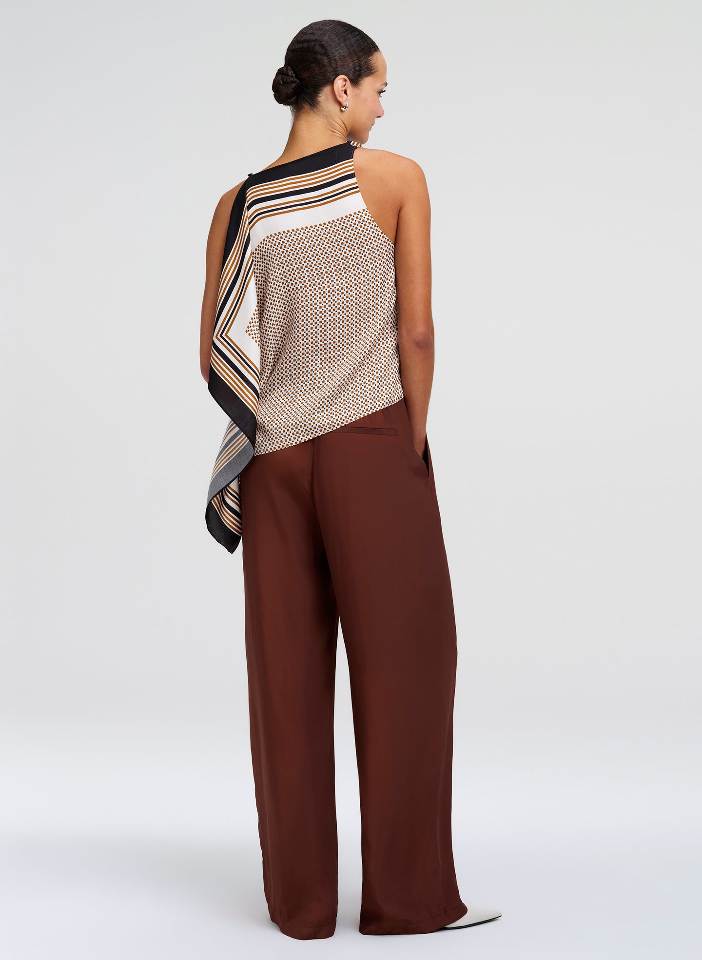 Woman wearing a patterned top and brown pants on a white background