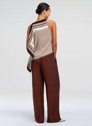 Woman wearing a patterned top and brown pants on a white background