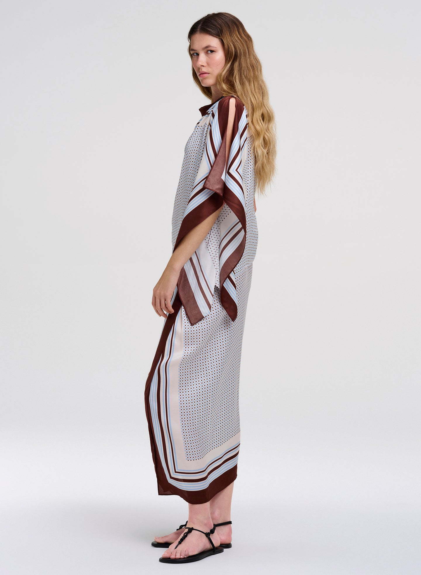 A woman modeling a matching top and skirt with a white base, brown and black striped border, and a subtle geometric pattern, photographed against a light gray studio background.