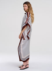 A woman modeling a matching top and skirt with a white base, brown and black striped border, and a subtle geometric pattern, photographed against a light gray studio background.