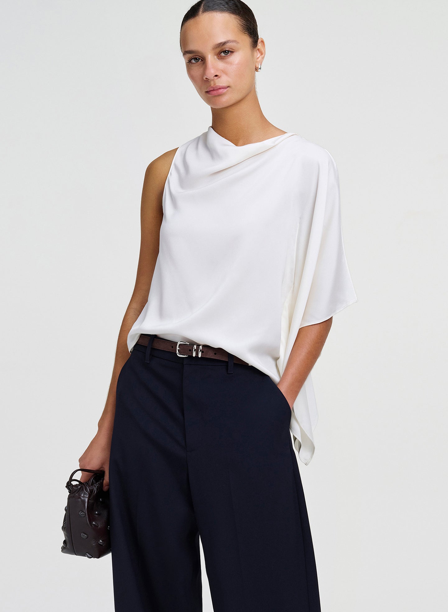 woman in white draped top and pants, holding leather bag