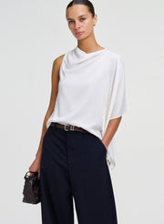 woman in white draped top and pants, holding leather bag