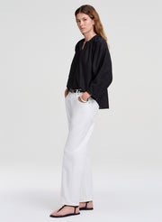 Woman wearing a black shirt and white pants on a plain background