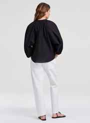 Person wearing a black blouse and white pants on a plain background