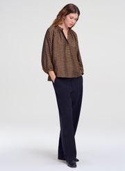 A woman modeling a brown and blue checkered long-sleeve blouse with dark navy wide-leg trousers, standing against a light gray studio background.