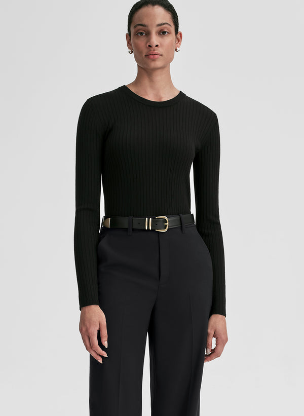 Person wearing a black ribbed long-sleeve top and black pants on a light gray background