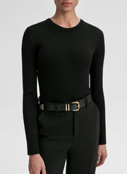 Person wearing a black ribbed long-sleeve top and black pants with a gold belt on a white background